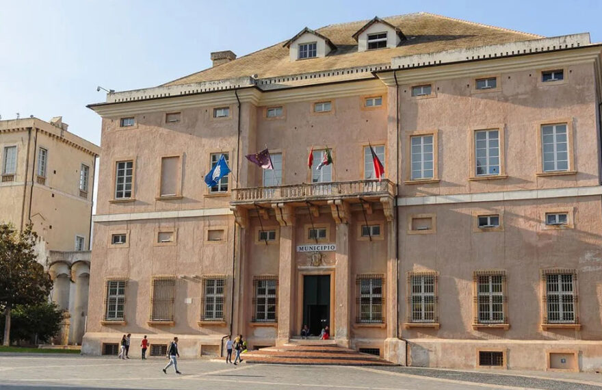 La facciata storica di Palazzo Doria, sede del Comune di Loano, con le bandiere istituzionali sul balcone e la piazza antistante.