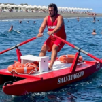 Bagnino rema su un pattino di salvataggio rosso in mare, con ciambella di salvataggio a bordo.
