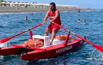 Bagnino rema su un pattino di salvataggio rosso in mare, con ciambella di salvataggio a bordo.