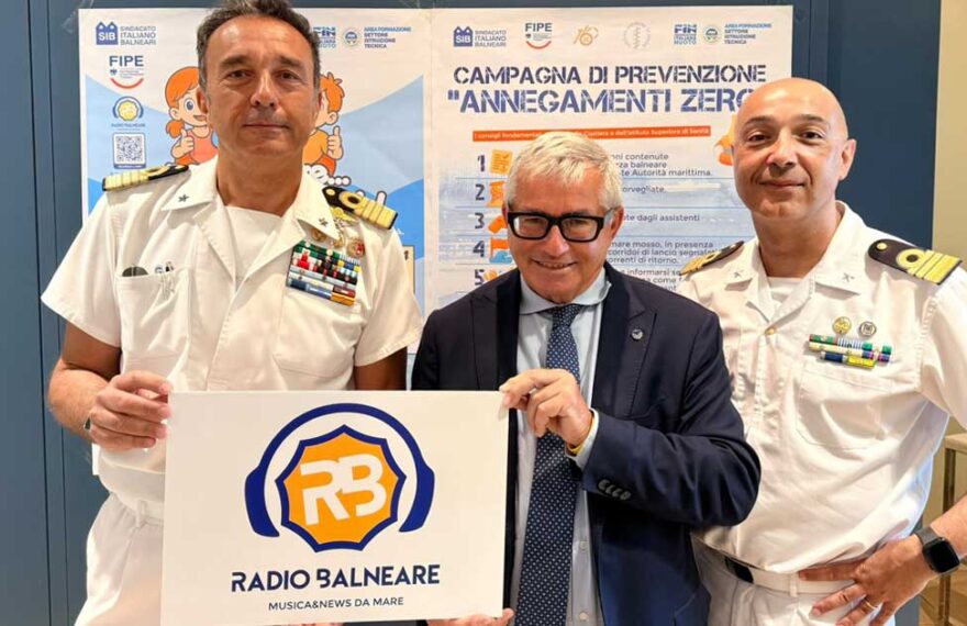Antonio Capacchione presidente SIB con ufficiali della Guardia Costiera mostra il logo di Radio Balneare alla presentazione della campagna Annegamenti Zero.