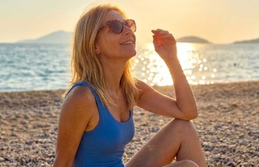 donna in costume da bagno con occhiali da sole seduta sulla spiaggia al tramonto