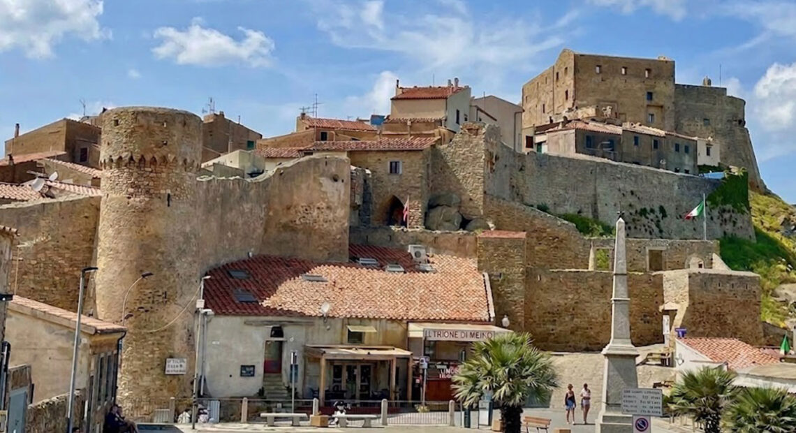 La maestosa Rocca Aldobrandesca e le mura storiche di Giglio Castello sotto un cielo azzurro con nuvole bianche