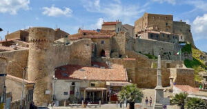 La maestosa Rocca Aldobrandesca e le mura storiche di Giglio Castello sotto un cielo azzurro con nuvole bianche