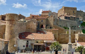 La maestosa Rocca Aldobrandesca e le mura storiche di Giglio Castello sotto un cielo azzurro con nuvole bianche