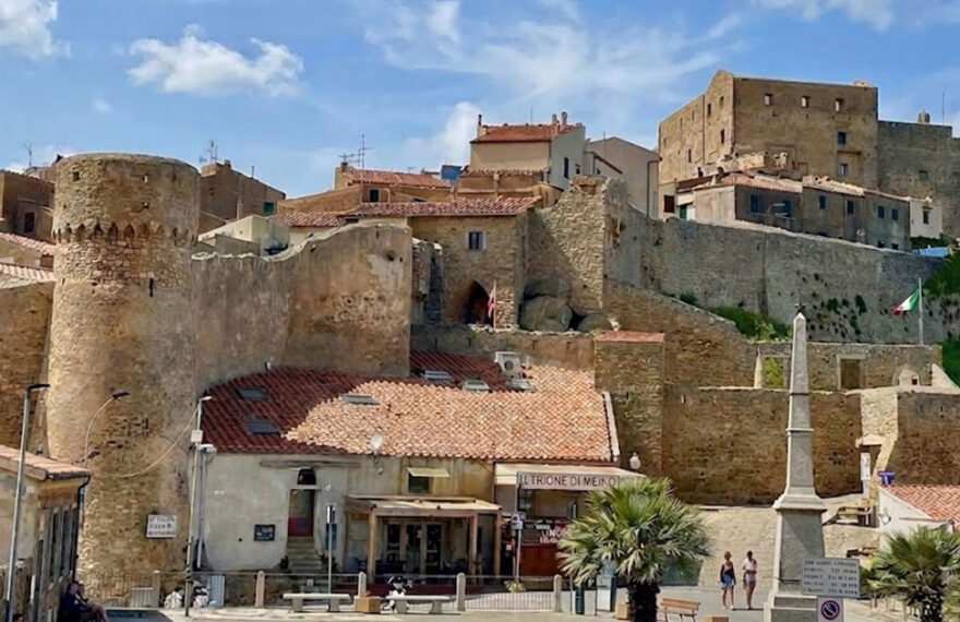 La maestosa Rocca Aldobrandesca e le mura storiche di Giglio Castello sotto un cielo azzurro con nuvole bianche