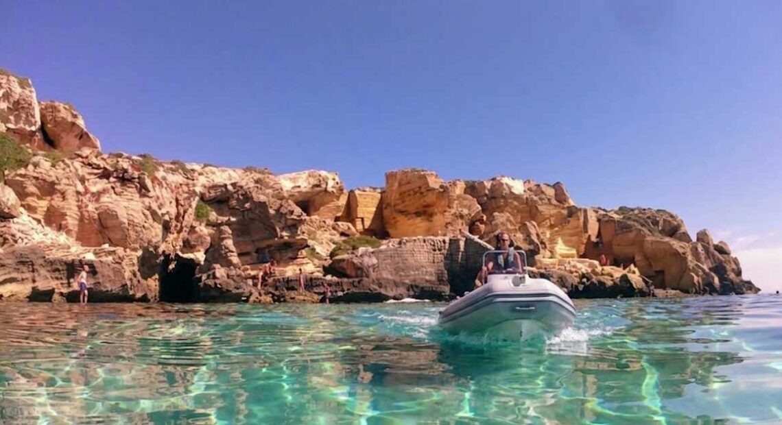 Un gommone naviga nel mare cristallino sotto le scogliere di tufo a Favignana