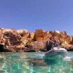 Un gommone naviga nel mare cristallino sotto le scogliere di tufo a Favignana