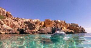 Un gommone naviga nel mare cristallino sotto le scogliere di tufo a Favignana