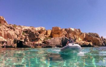 Un gommone naviga nel mare cristallino sotto le scogliere di tufo a Favignana