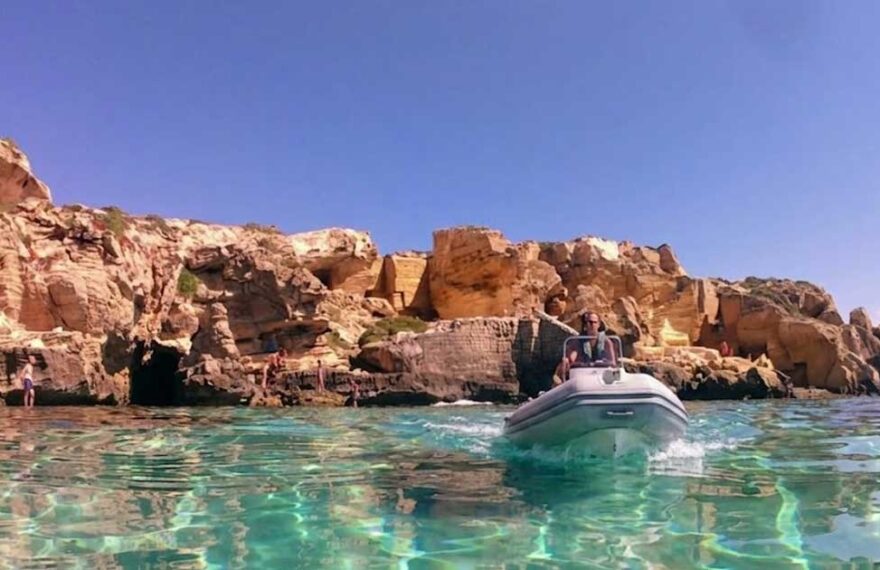 Un gommone naviga nel mare cristallino sotto le scogliere di tufo a Favignana