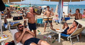 Una scena balneare caotica e affollata in Italia, che illustra vari comportamenti fastidiosi dei bagnanti citati nel decalogo del bon ton del Codacons, come l'uso di telefoni, musica ad alto volume, fumo e rumore.