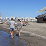 Una coppia cammina sul bagnasciuga della spiaggia di Ladispoli con stabilimento balneare in legno sullo sfondo