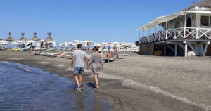 Una coppia cammina sul bagnasciuga della spiaggia di Ladispoli con stabilimento balneare in legno sullo sfondo