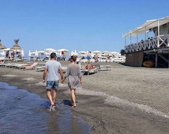 Una coppia cammina sul bagnasciuga della spiaggia di Ladispoli con stabilimento balneare in legno sullo sfondo