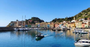 Vista panoramica del molo e delle case colorate di Giglio Porto con barche ormeggiate e acqua cristallina.