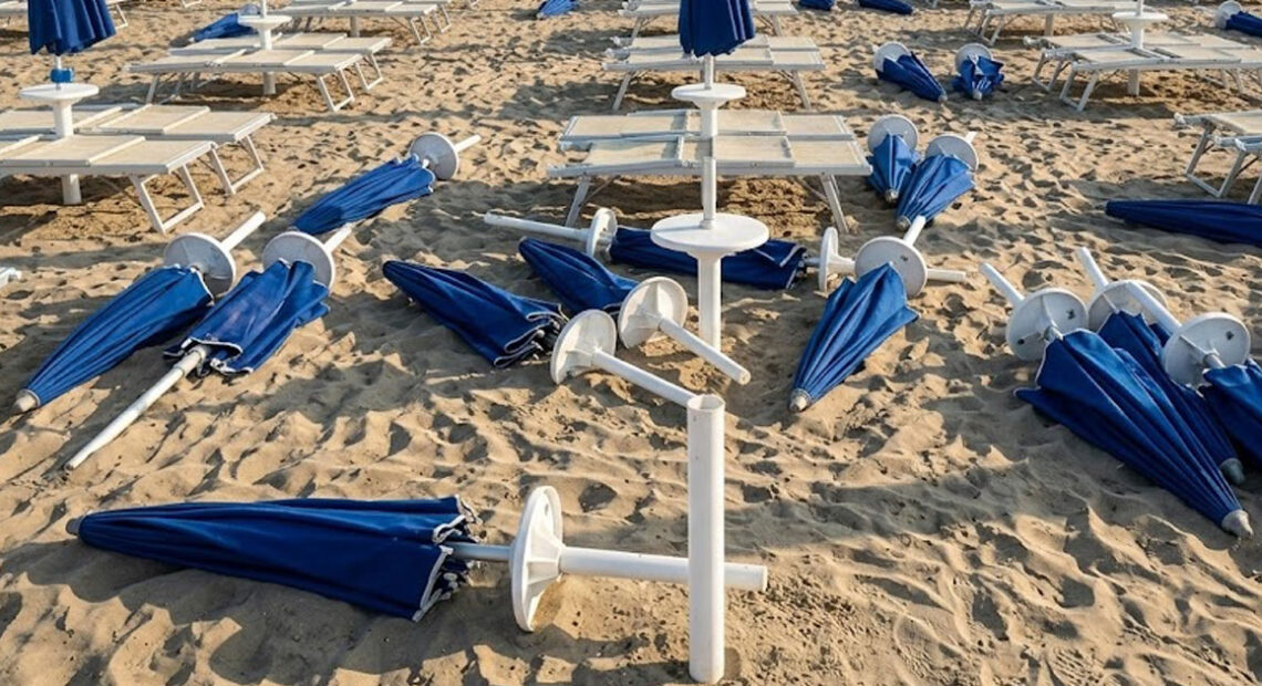 Spiaggia devastata dai maranza al Bagno Holiday di Lido di Spina, con ombrelloni blu sradicati e lettini rovesciati sulla sabbia