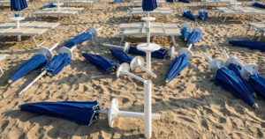 Spiaggia devastata dai maranza al Bagno Holiday di Lido di Spina, con ombrelloni blu sradicati e lettini rovesciati sulla sabbia