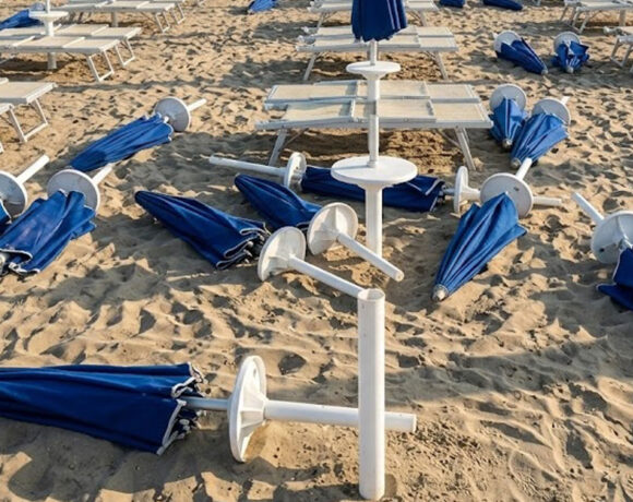 Spiaggia devastata dai maranza al Bagno Holiday di Lido di Spina, con ombrelloni blu sradicati e lettini rovesciati sulla sabbia