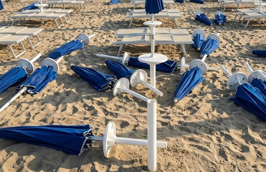 Spiaggia devastata dai maranza al Bagno Holiday di Lido di Spina, con ombrelloni blu sradicati e lettini rovesciati sulla sabbia