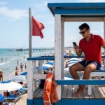 Assistente bagnanti in torretta di salvataggio mentre utilizza lo smartphone durante il servizio di vigilanza in spiaggia.