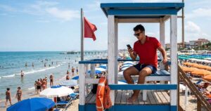 Assistente bagnanti in torretta di salvataggio mentre utilizza lo smartphone durante il servizio di vigilanza in spiaggia.