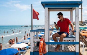 Assistente bagnanti in torretta di salvataggio mentre utilizza lo smartphone durante il servizio di vigilanza in spiaggia.
