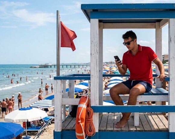 Assistente bagnanti in torretta di salvataggio mentre utilizza lo smartphone durante il servizio di vigilanza in spiaggia.