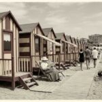 Ricostruzione d'epoca di una fila di cabine balneari in legno a righe sulla spiaggia con bagnanti nei primi del Novecento.