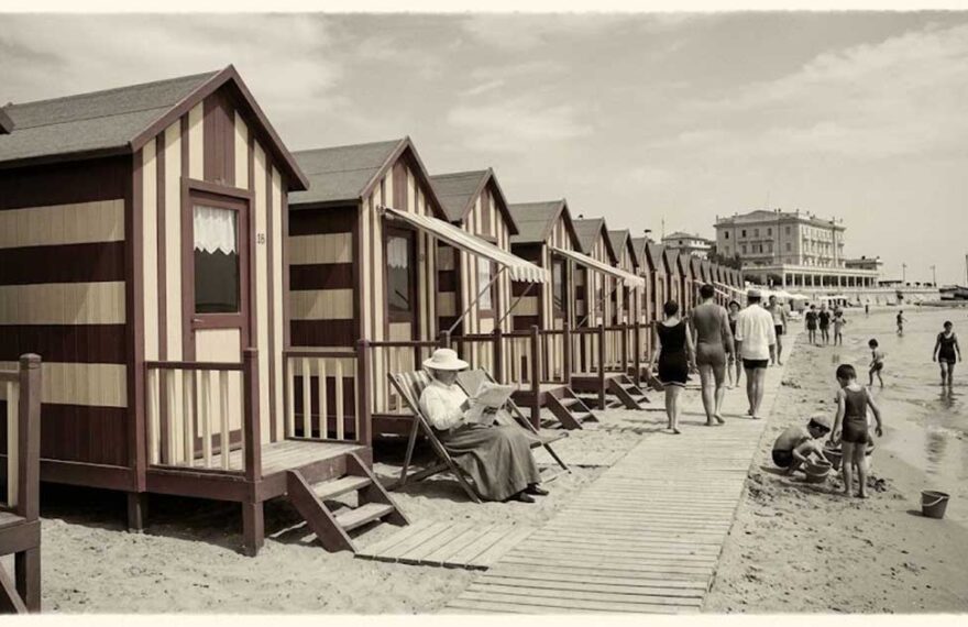 Ricostruzione d'epoca di una fila di cabine balneari in legno a righe sulla spiaggia con bagnanti nei primi del Novecento.