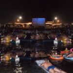 Spettatori in mare su materassini e gonfiabili mentre guardano il film Lo Squalo sul bagnasciuga di Fano.