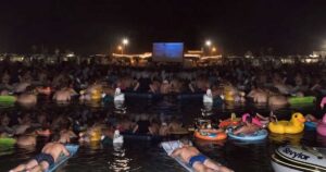 Spettatori in mare su materassini e gonfiabili mentre guardano il film Lo Squalo sul bagnasciuga di Fano.