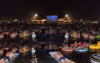 Spettatori in mare su materassini e gonfiabili mentre guardano il film Lo Squalo sul bagnasciuga di Fano.