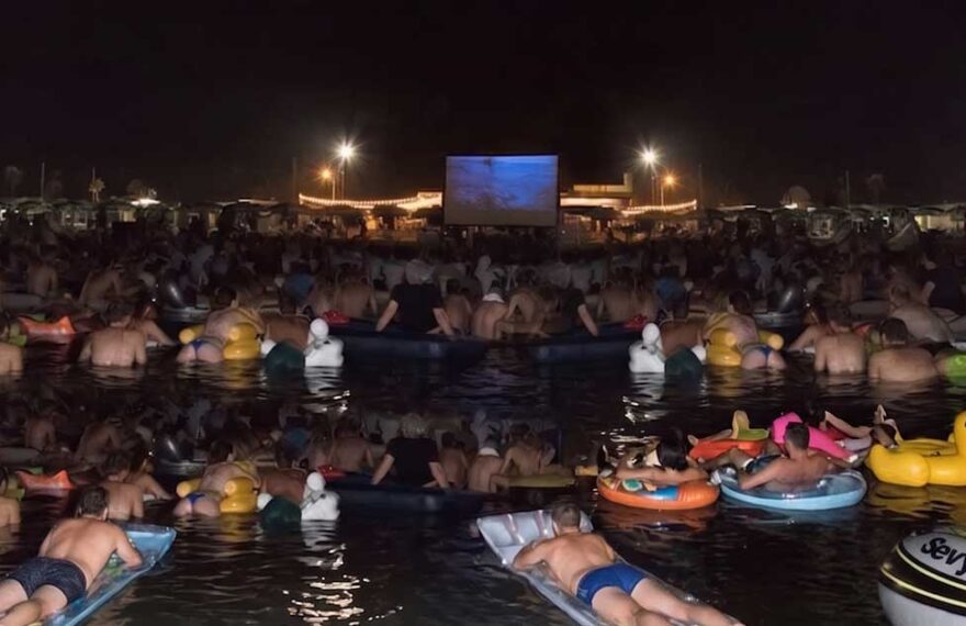 Spettatori in mare su materassini e gonfiabili mentre guardano il film Lo Squalo sul bagnasciuga di Fano.