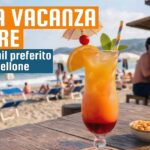 Un bicchiere di cocktail esotico (Tequila Sunrise) con frutta e ombrellino su un tavolo di legno in una spiaggia italiana affollata, con scritte sovrapposte "La tua vacanza da bere" e "il tuo cocktail preferito sotto l'ombrellone".