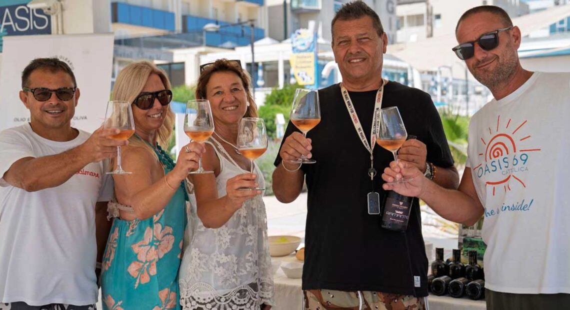 Un gruppo di persone brinda con calici di vino durante un'iniziativa di degustazione in spiaggia a Cattolica.
