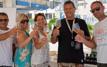 Un gruppo di persone brinda con calici di vino durante un'iniziativa di degustazione in spiaggia a Cattolica.