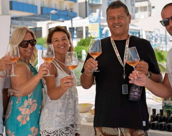 Un gruppo di persone brinda con calici di vino durante un'iniziativa di degustazione in spiaggia a Cattolica.