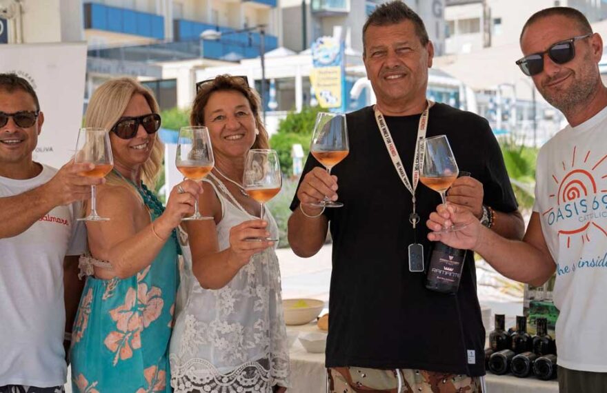 Un gruppo di persone brinda con calici di vino durante un'iniziativa di degustazione in spiaggia a Cattolica.