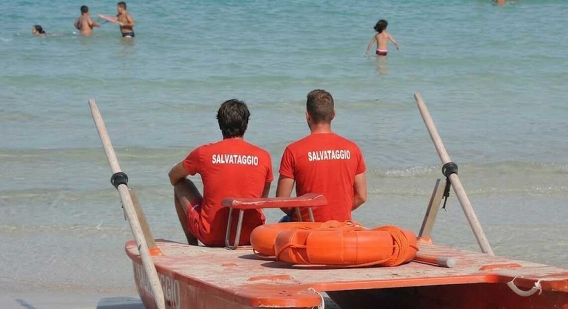 Due bagnini di salvataggio in maglietta rossa seduti su un pattino di salvataggio di fronte al mare