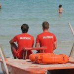 Due bagnini di salvataggio in maglietta rossa seduti su un pattino di salvataggio di fronte al mare