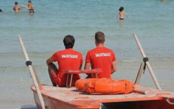 Due bagnini di salvataggio in maglietta rossa seduti su un pattino di salvataggio di fronte al mare