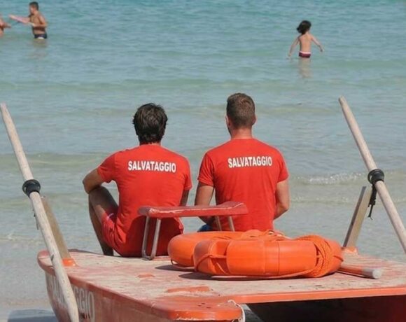 Due bagnini di salvataggio in maglietta rossa seduti su un pattino di salvataggio di fronte al mare