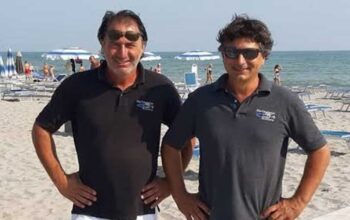 Gilberto e Cesare Fuzzi, gestori dei Bagni 54 Nino e Nando di Riccione, sorridenti in spiaggia.