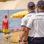 Militari della Guardia Costiera in divisa effettuano controlli tra gli ombrelloni in uno stabilimento balneare.