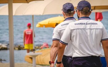 Militari della Guardia Costiera in divisa effettuano controlli tra gli ombrelloni in uno stabilimento balneare.