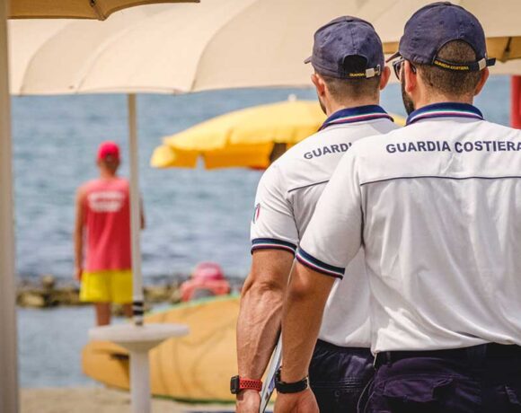 Militari della Guardia Costiera in divisa effettuano controlli tra gli ombrelloni in uno stabilimento balneare.