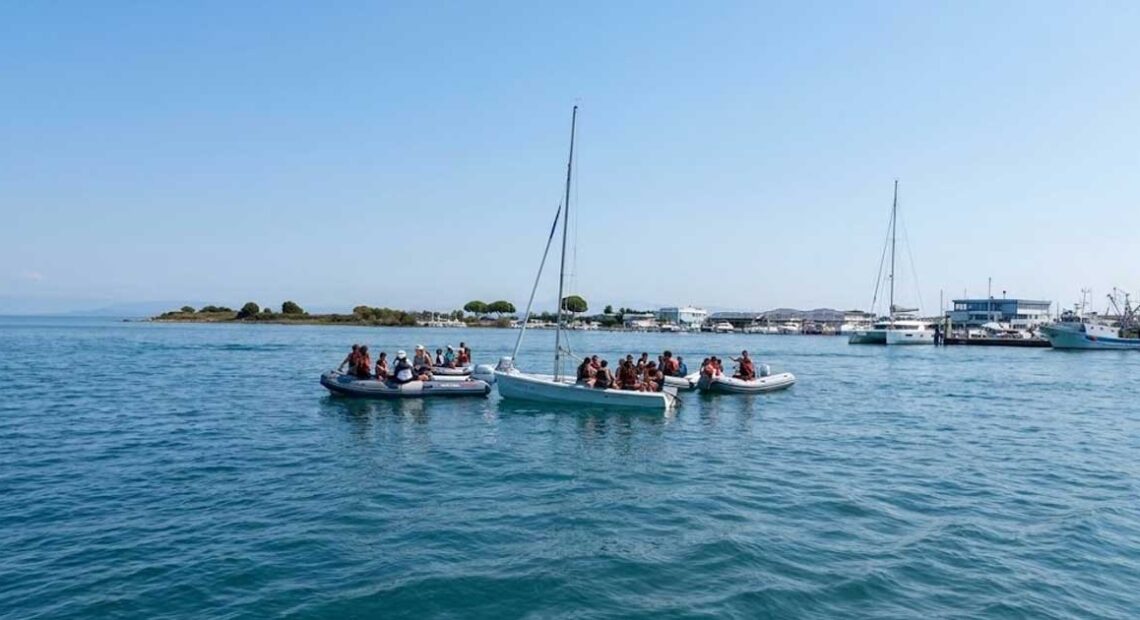 Giovani allievi della scuola di vela con giubbotto salvagente seduti a bordo di una barca a vela nel mare di Grado