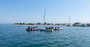Giovani allievi della scuola di vela con giubbotto salvagente seduti a bordo di una barca a vela nel mare di Grado