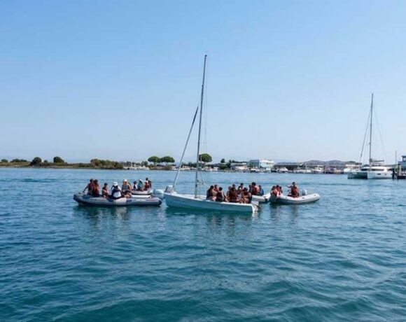 Giovani allievi della scuola di vela con giubbotto salvagente seduti a bordo di una barca a vela nel mare di Grado