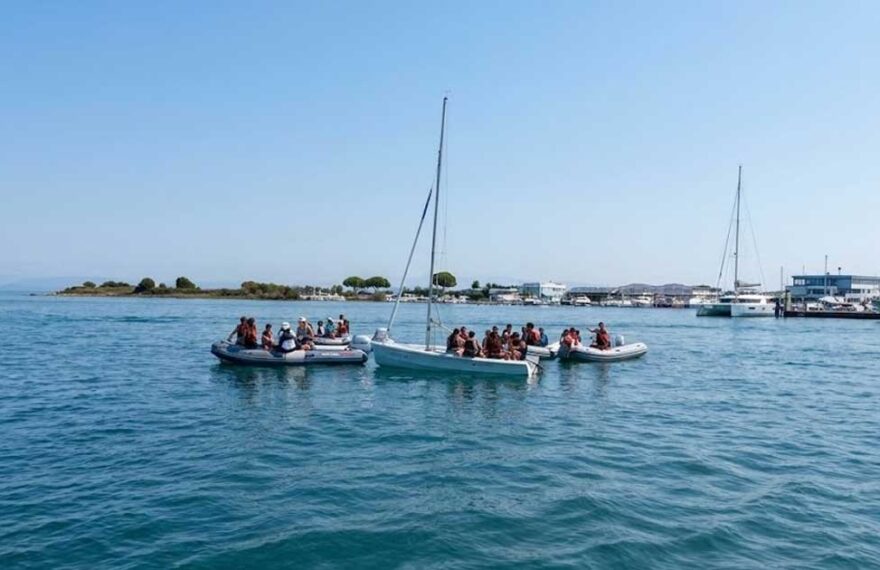 Giovani allievi della scuola di vela con giubbotto salvagente seduti a bordo di una barca a vela nel mare di Grado
